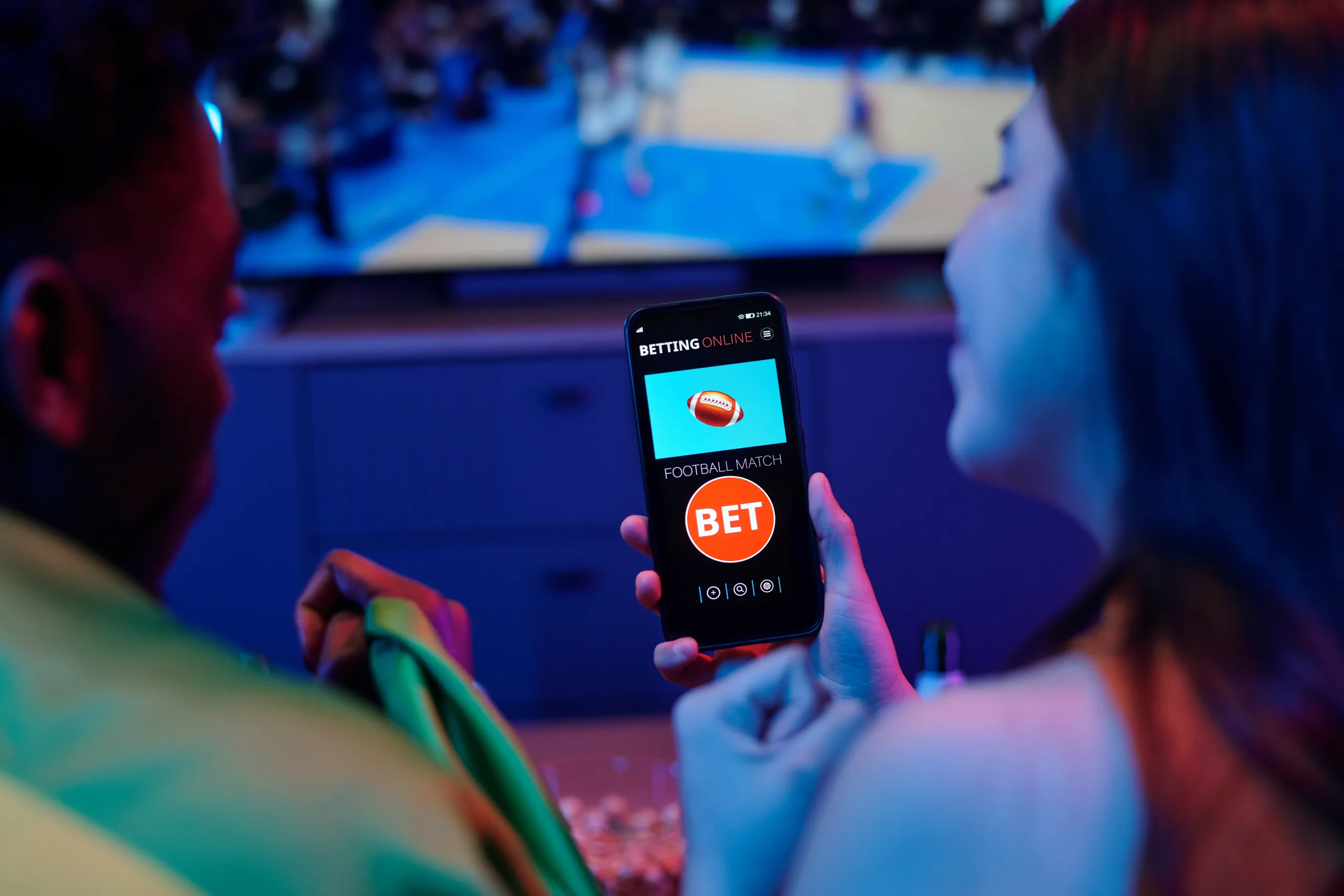 Young Caucasian Woman and Black Man Using Smartphone for Online Sports Betting