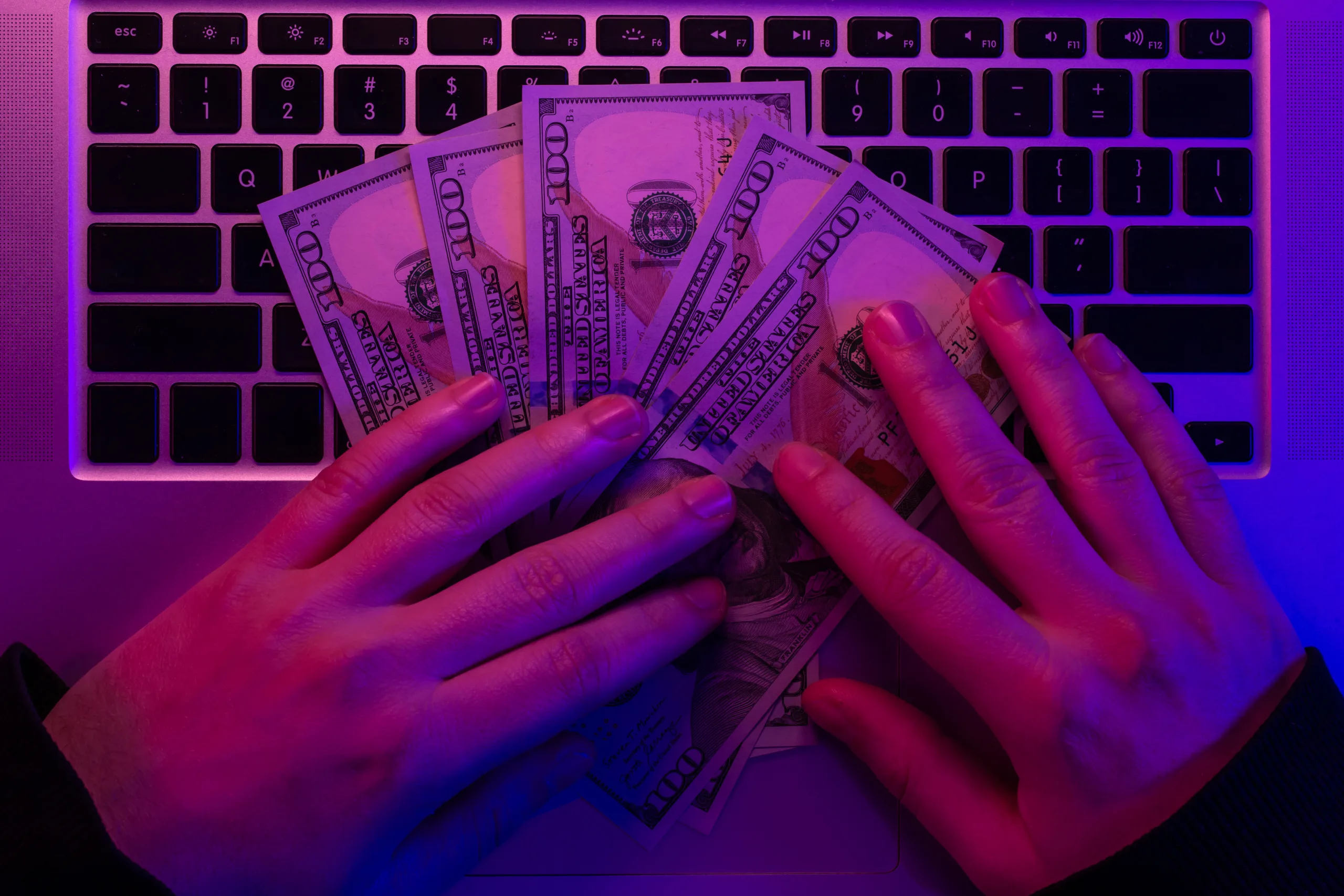 Money in male hands on the background of a laptop keyboard in neon lighting.
