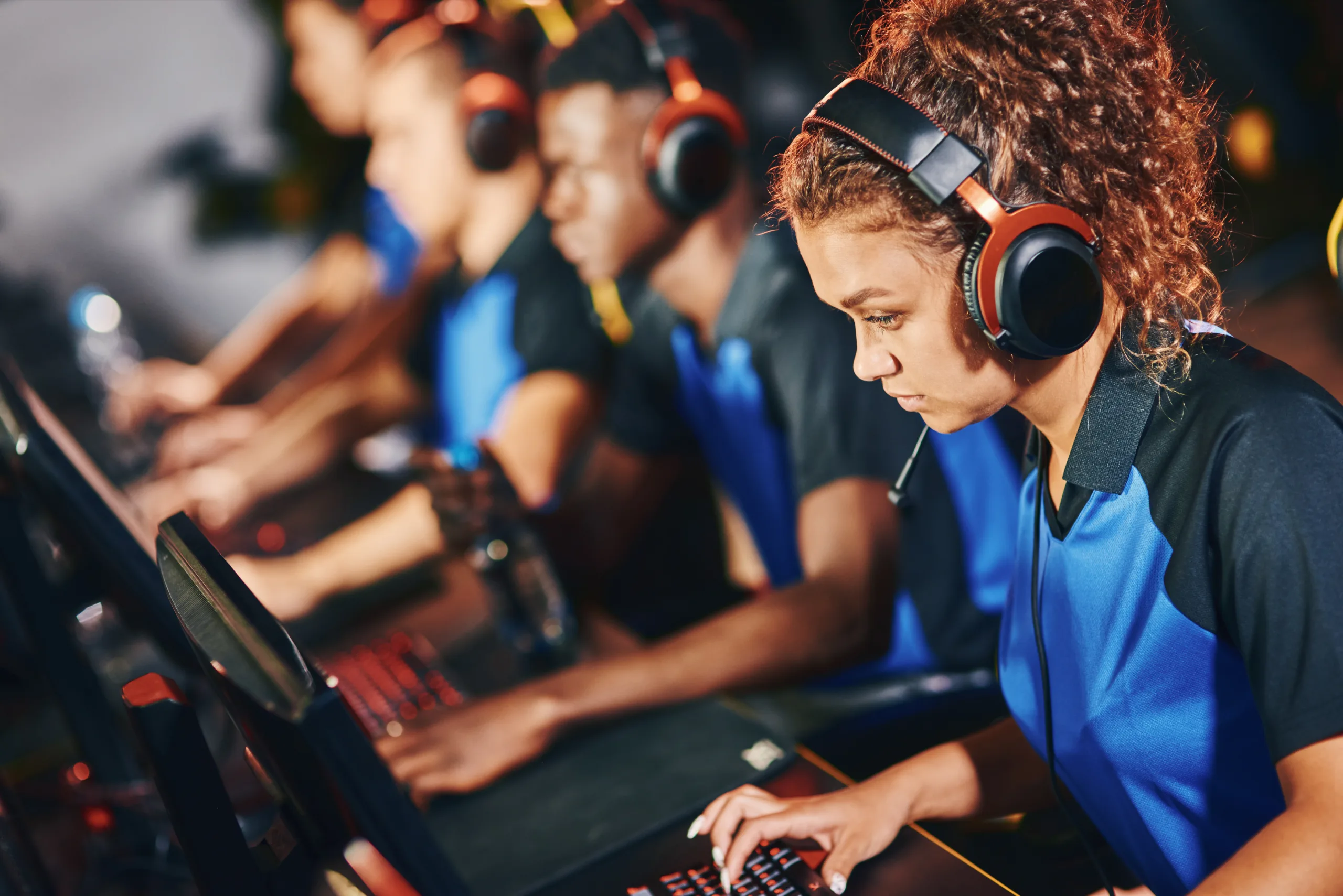 Focused female cybersport gamer wearing headphones participating in eSport tournament, sitting in a row with other team members and playing online video games
